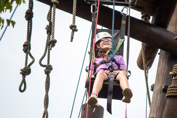 Girl in chair harness at top of climbing tower