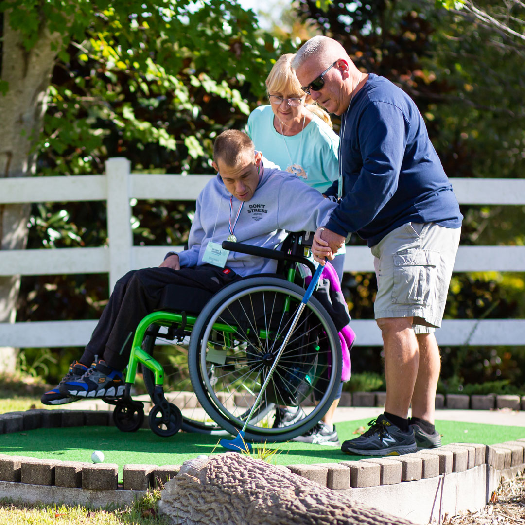 Boy in wheelchair with two volunteers playing mini-golf