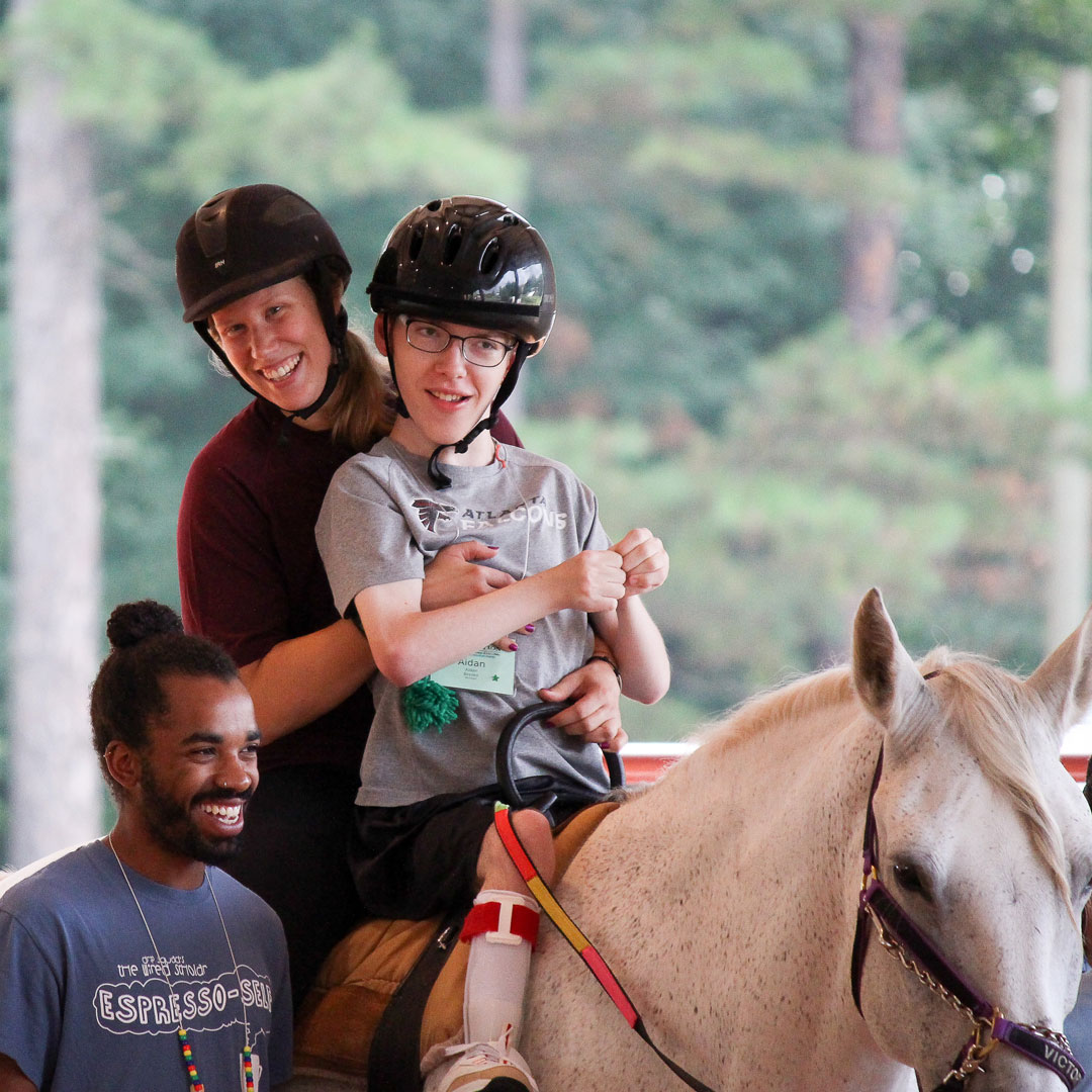 Boy and barn director riding horseback with counselor providing extra support