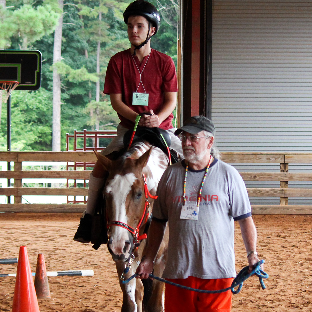 Volunteer leading a camper on horseback.