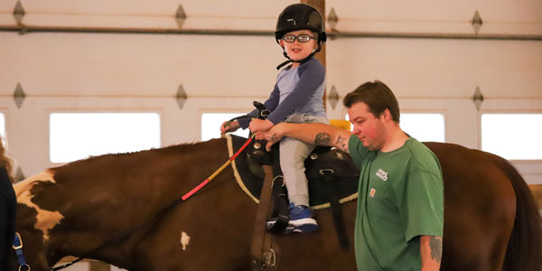 Boy riding horse during horseback riding therapy session.