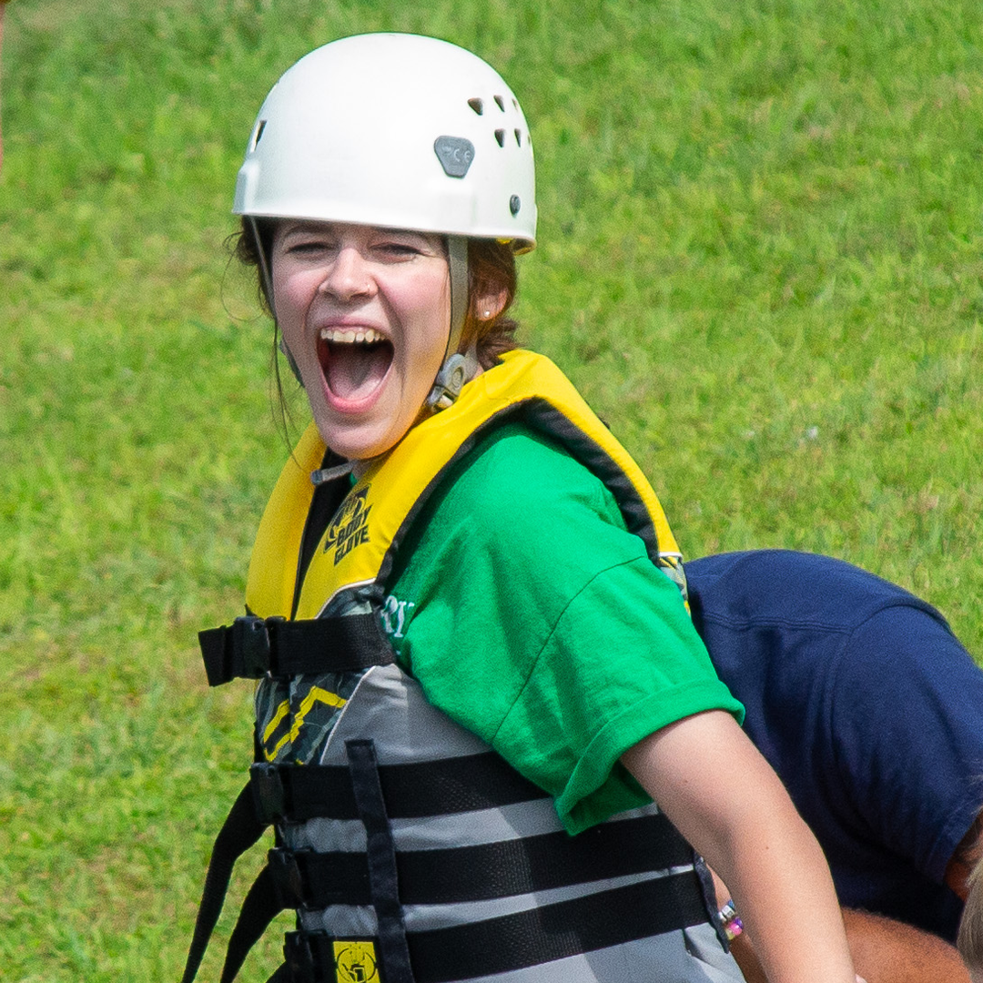 Bailey wearing a helmet and life vest. She is laughing.