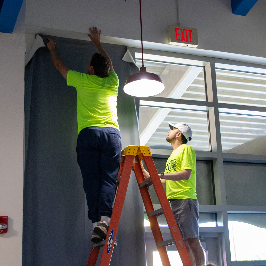 Volunteers install light-blocking panels over the windows in the Arts & Crafts building.
