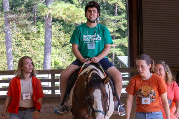 Camper riding a horse with staff support at Victory Junction.
