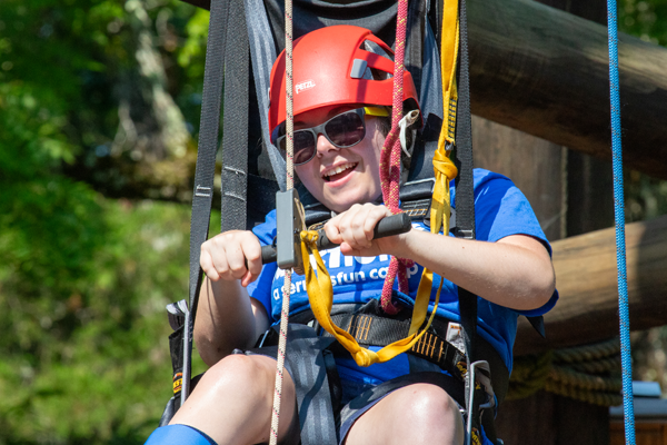 Camper wearing a helmet and harness smiles while participating in a zip line activity.