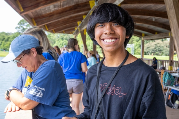Camp Memories Banner Image 2 600x400 Camper smiling at the camera on a lakeside dock at Victory Junction.