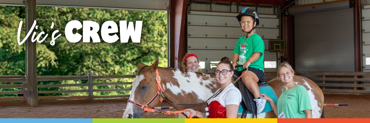 Camper rides a horse with staff support inside the camp barn.